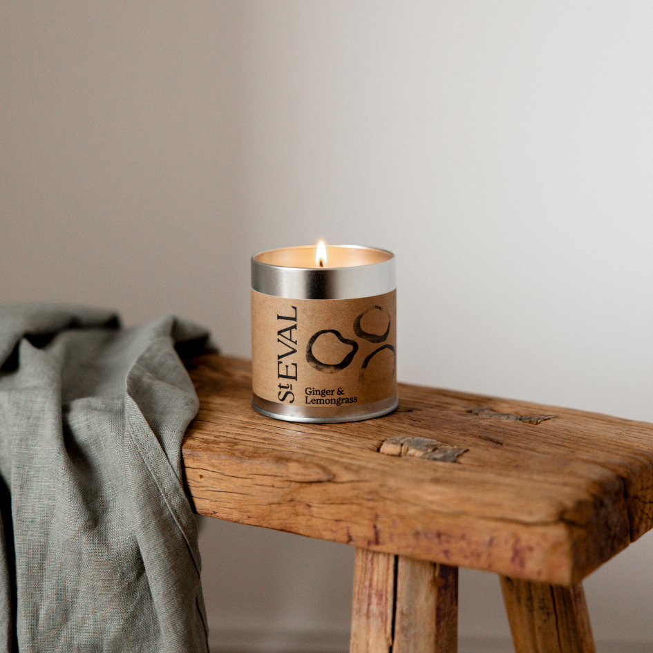 Candle with 'St EVAL' branding on a rustic wooden bench with plain background
