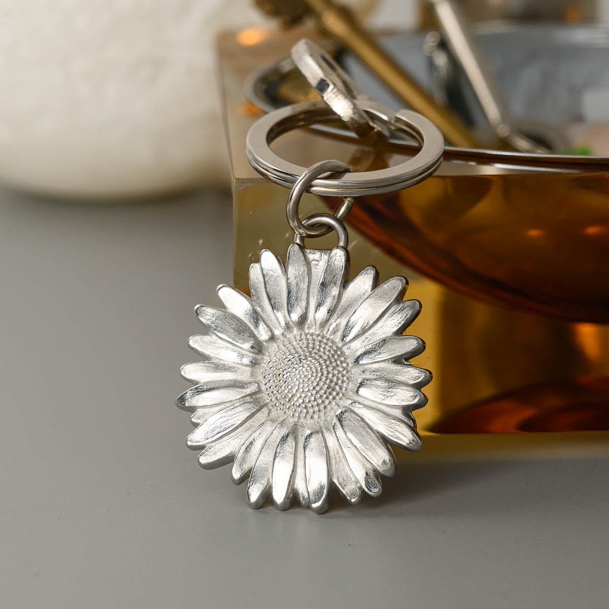 Silver sunflower-shaped keychain on a gray surface with a blurred background