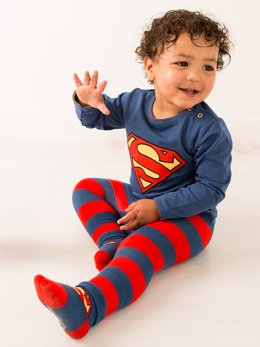 Child wearing a Superman outfit with a blue shirt and red and blue striped pants on a white background