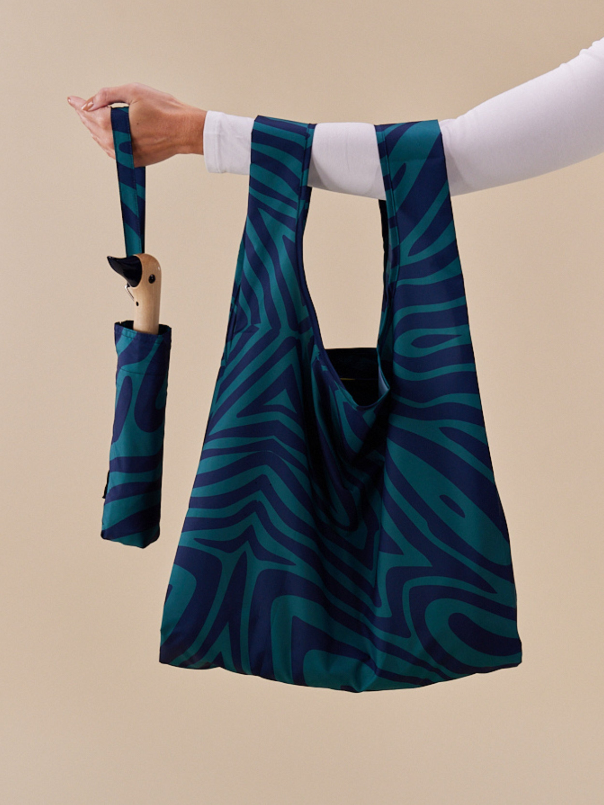 Person holding a blue patterned reusable bag with a matching umbrella on a beige background